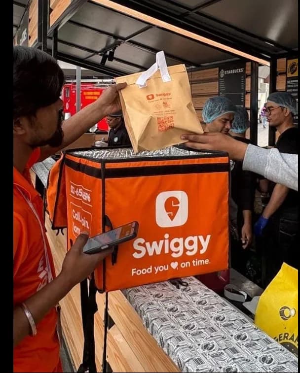 Swiggy delivery partner handing over a food order to a customer at a restaurant pickup point.