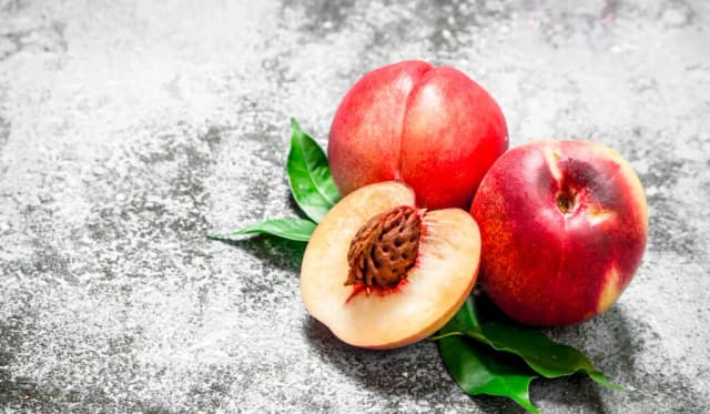 Fresh whole and sliced peaches with green leaves on rustic background